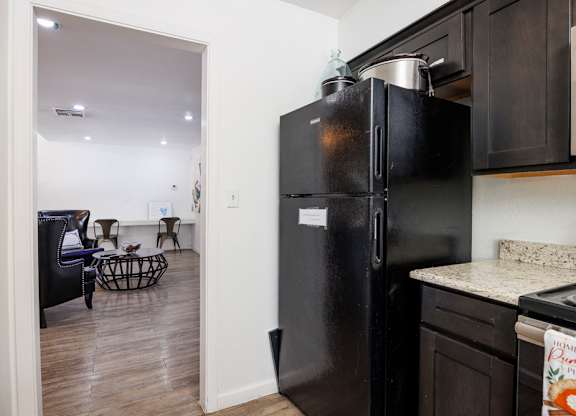 A black refrigerator is in a kitchen with a dining table and chairs in the background.