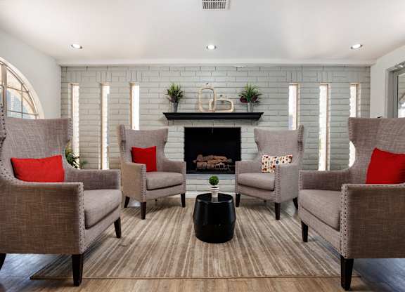 Four chairs with red pillows are arranged around a fireplace.