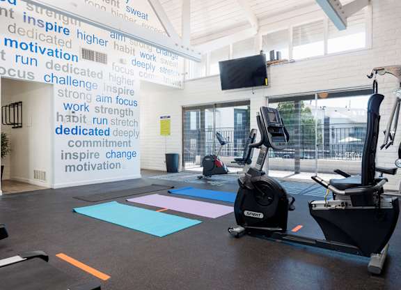 A gym with a wall of motivational words and exercise equipment.
