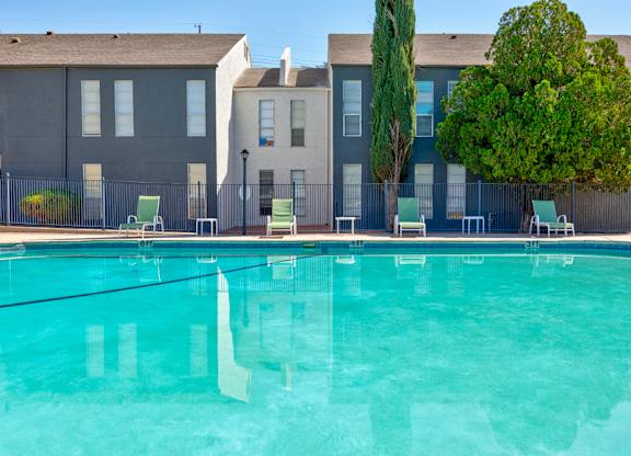 A swimming pool in front of a building with trees and chairs around it.