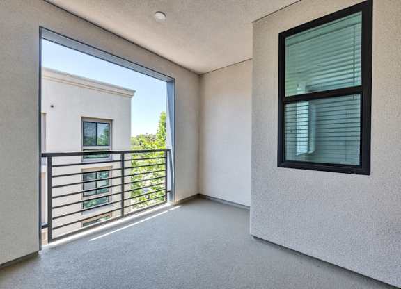 A balcony with a metal railing and a window overlooking a building.