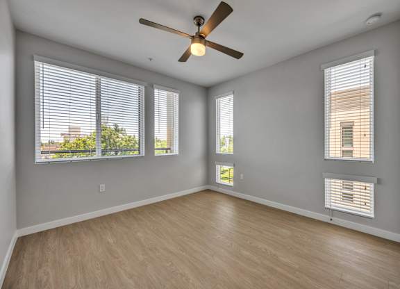 A room with a ceiling fan and two windows.