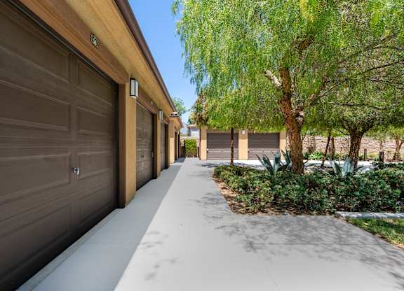 A long driveway with a row of garage doors on one side and a tree on the other.