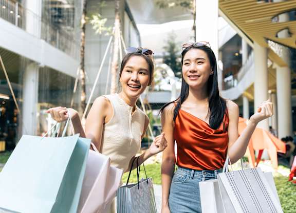 Two women holding shopping bags in front of a building.