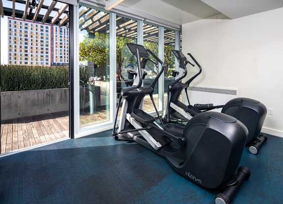 A treadmill and a stationary bike are in a room with a view of a city.