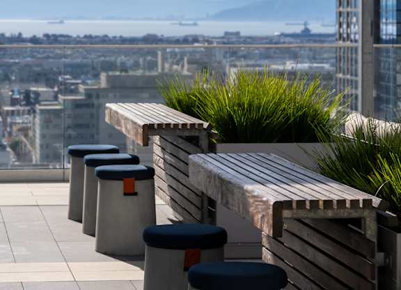 A row of grey concrete bins with black lids are lined up on a rooftop terrace.