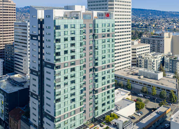 A tall building with a red logo on the side is surrounded by other buildings.