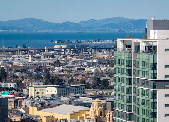 A cityscape with a mix of modern and older buildings, with a body of water and mountains in the distance.