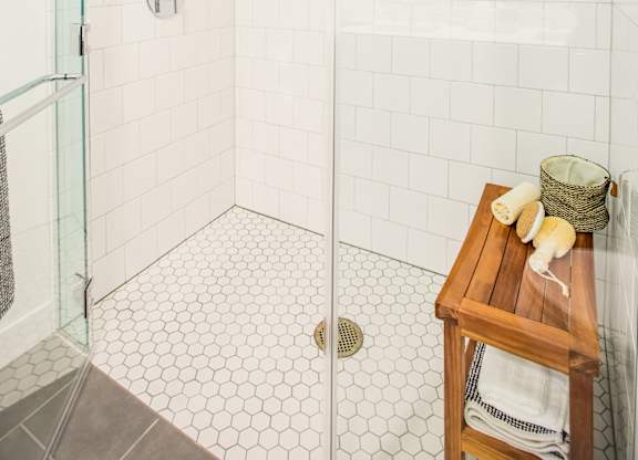 A white tiled shower with a glass door and a wooden stool with towels on it.at The Rise, San Francisco, CA  
