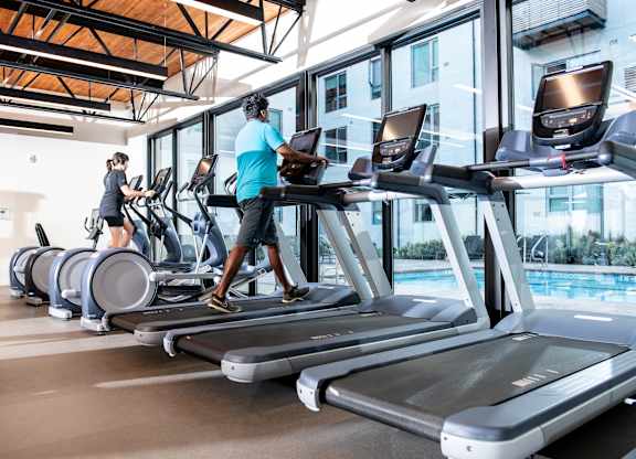 A gym with people exercising on treadmills and elliptical machines.