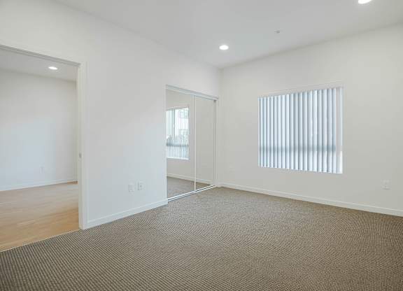 A large empty room with a carpeted floor and a window with blinds.