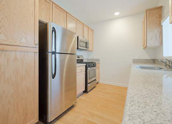 A kitchen with a stainless steel refrigerator and wooden cabinets.