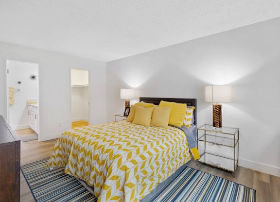 A bedroom with a bed covered in yellow and white bedding at Verandas Apartments, West Covina, California