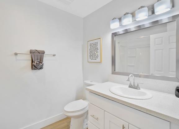 A white bathroom with a toilet, sink, mirror, and a towel rack at Verandas Apartments, West Covina, 91791