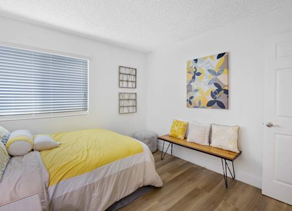 A bedroom with a bed, bench, and artwork at Verandas Apartments, West Covina, California