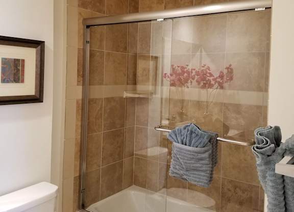 A bathroom with a toilet, a shower with a glass door, and towels hanging on a rack at Woodley Sara Apartment, Van Nuys, CA, 91406
