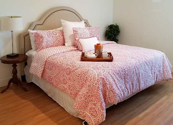 A bed with a red and white patterned comforter and matching pillow cases sits in a room with wooden flooring and white walls at Woodley Sara Apartment, Van Nuys, CA