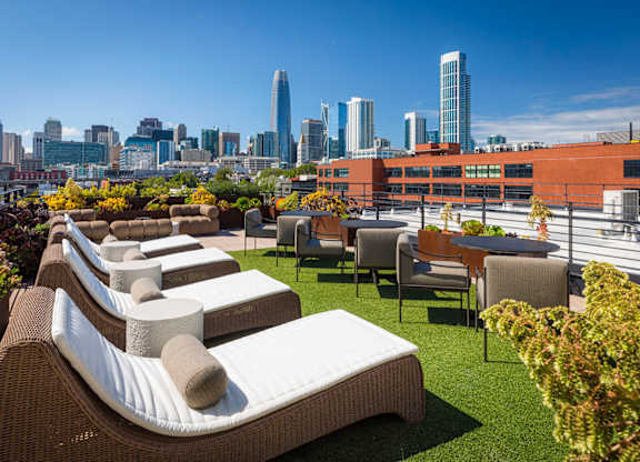 A rooftop patio with wicker chairs and cushions overlooking a city skyline.