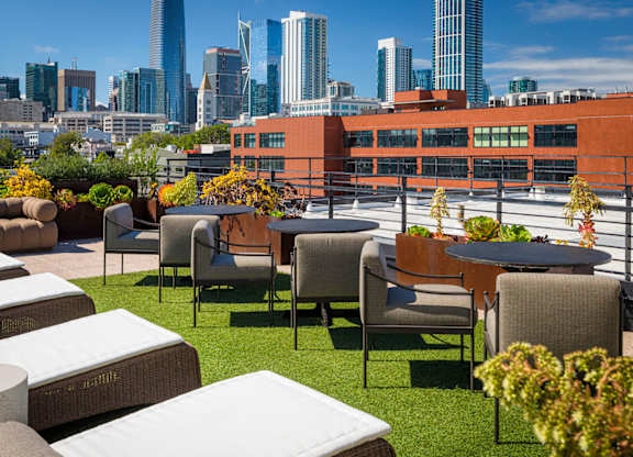 A rooftop patio with white cushioned seating and green plants.