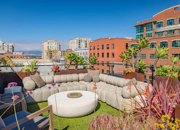 A modern outdoor seating area with a large white circular table surrounded by cushions and plants.