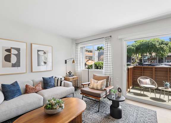 A living room with a grey couch, a wooden table, and a view of the outside.