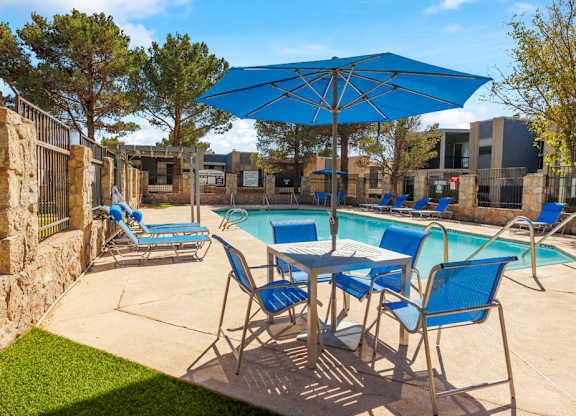 A pool area with blue chairs and an umbrella.
