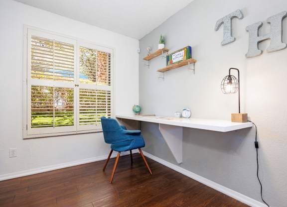 A room with a desk, chair, and shelves with plants.