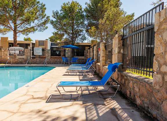 A pool with blue chairs and a stone wall.