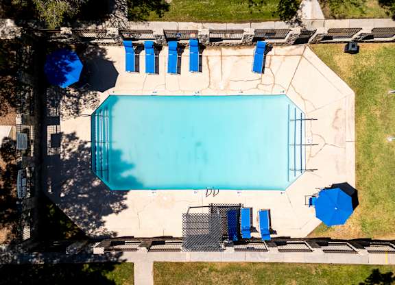 An aerial view of a swimming pool surrounded by blue lounge chairs and umbrellas.