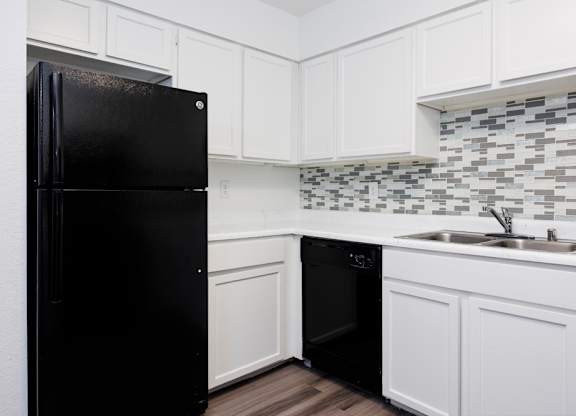 A black refrigerator in a kitchen with white cabinets and a black dishwasher.