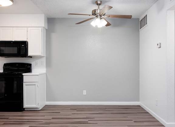A kitchen with a black microwave and oven, white cabinets, and a ceiling fan.