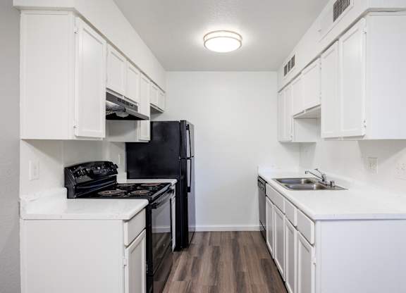 A black refrigerator is in a kitchen with white cabinets.