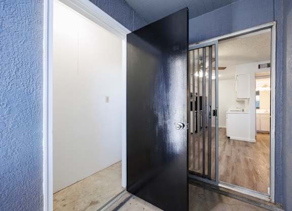 A black door with a glass window is open to a room with a white fridge.