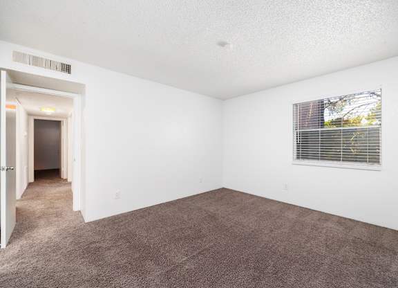 A room with a carpeted floor and a window with blinds.