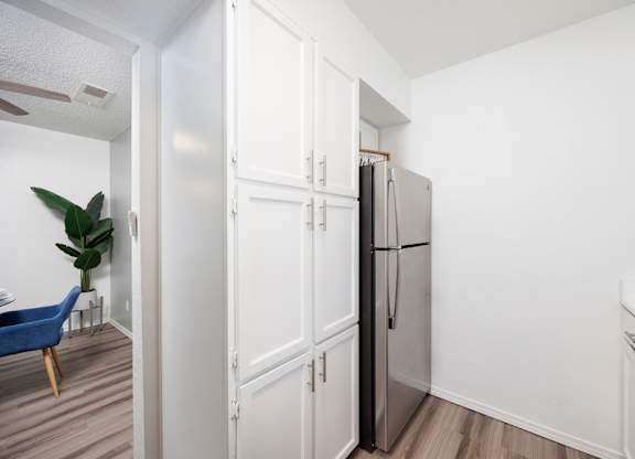 A kitchen with a refrigerator, a chair, and a plant.