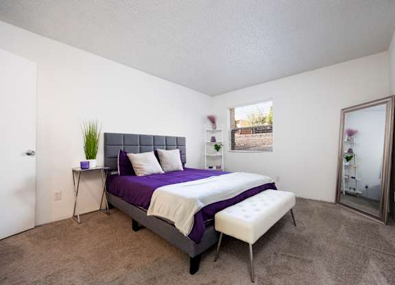 A bedroom with a purple bed and a white chair.