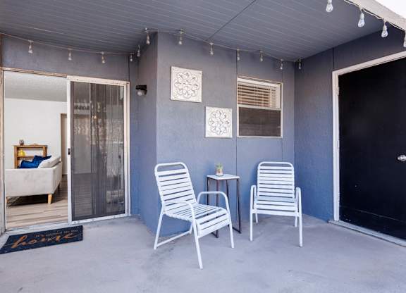 Two white chairs and a table are on a patio.