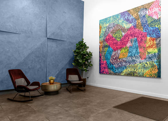 A colorful abstract painting hangs on a wall next to two chairs and a small table.