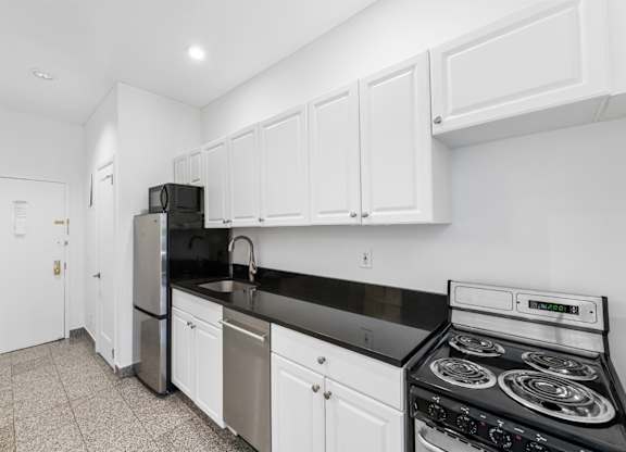 A kitchen with white cabinets and black countertops.