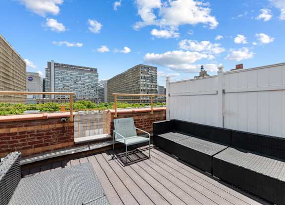 A wooden deck with a chair and a table in the foreground and a city skyline in the background.