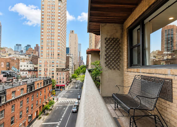 A black metal chair sits on a balcony overlooking a city street.