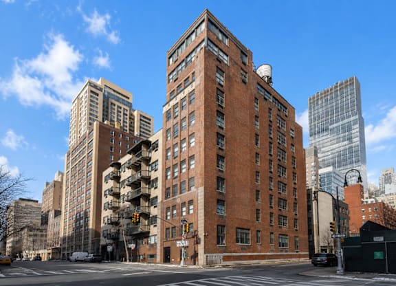 A large red brick building is in the middle of a city street.