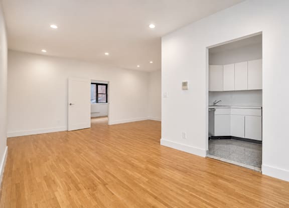 A room with wooden floors and a small kitchen area in the back.