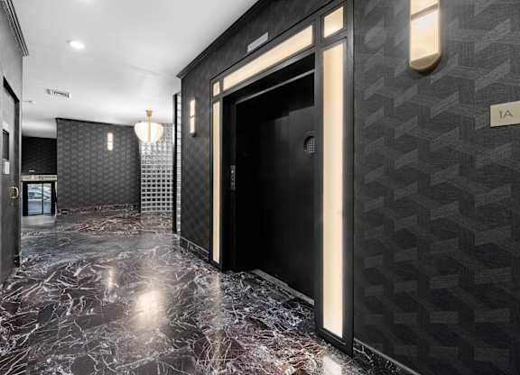 A hallway with a marble floor and a black door.