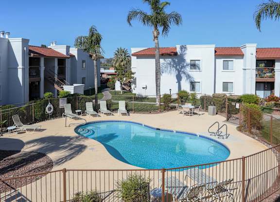 A pool surrounded by a fence and chairs in front of a white building.