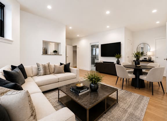 A modern living room with a white sofa, a black coffee table, and a TV mounted on the wall.