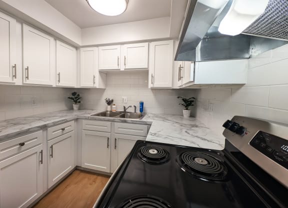 a kitchen with white cabinets and marble counter tops and a black stove top oven