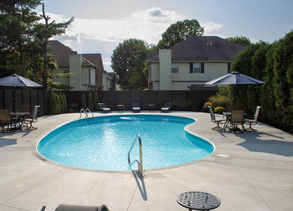 a swimming pool in a backyard with chairs and umbrellas