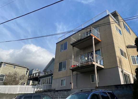 A car is parked in front of a tan apartment building with a balcony.