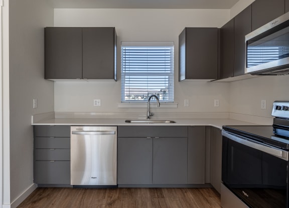 an empty kitchen with gray cabinets and stainless steel appliances and a window at Sagecrest Apartments, Wenatchee, Washington